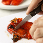 Photograph of chef scraping off pepper skin with knife.