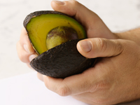 Photograph of twisting the halves of a cut avocado.